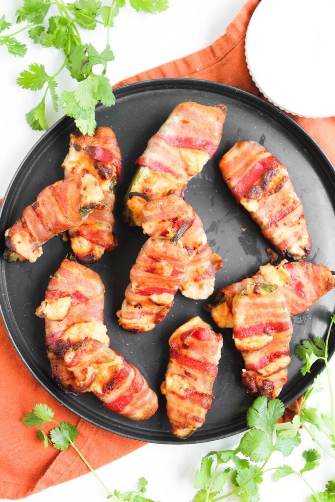 Ary fryer bacon wrapped jalapeno poppers arranged on a black plate.