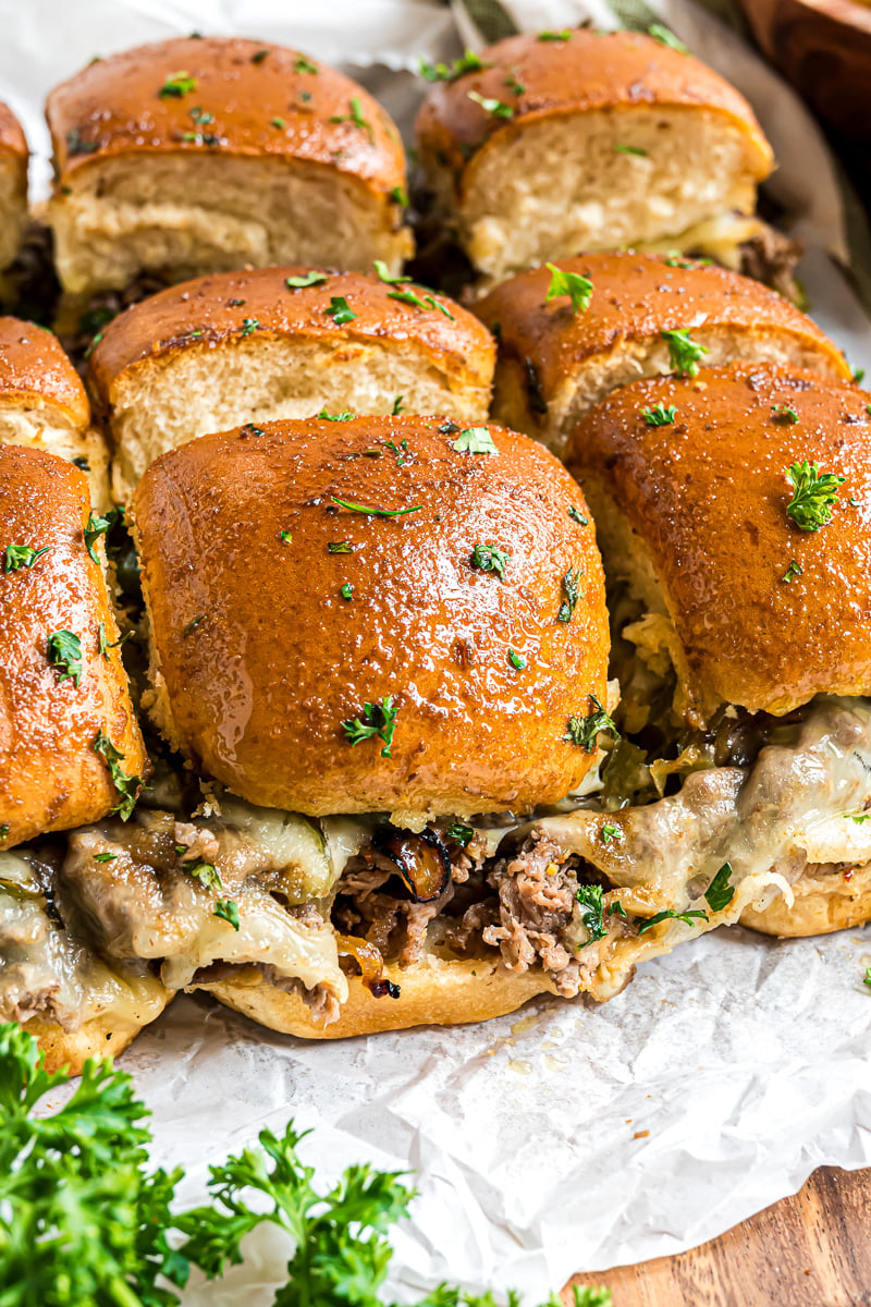 Philly cheesesteak sliders on a parchment lined serving board.