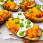 Buffalo chicken potato skins garnished with sour cream and green onions on parchment paper.