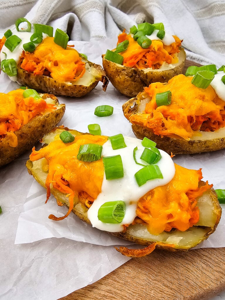 Buffalo chicken potato skins garnished with sour cream and green onions on parchment paper.
