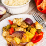 Sheet pan Hawaiian chicken served on a plate with a bowl of white rice for serving in the background.