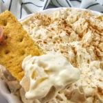 Apple dip in a bowl is dipped into with a Graham cracker.
