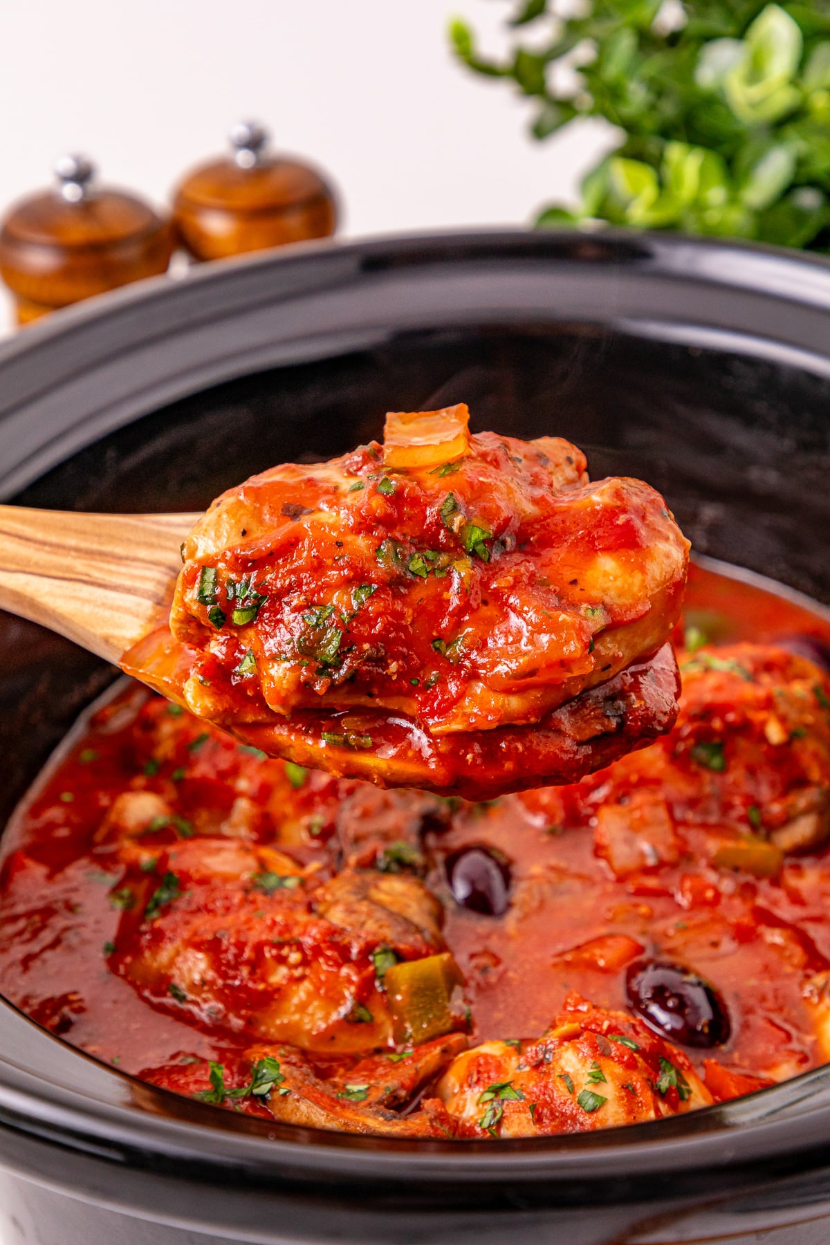 Crockpot chicken cacciatore scooped up on a spoon held over crockpot.