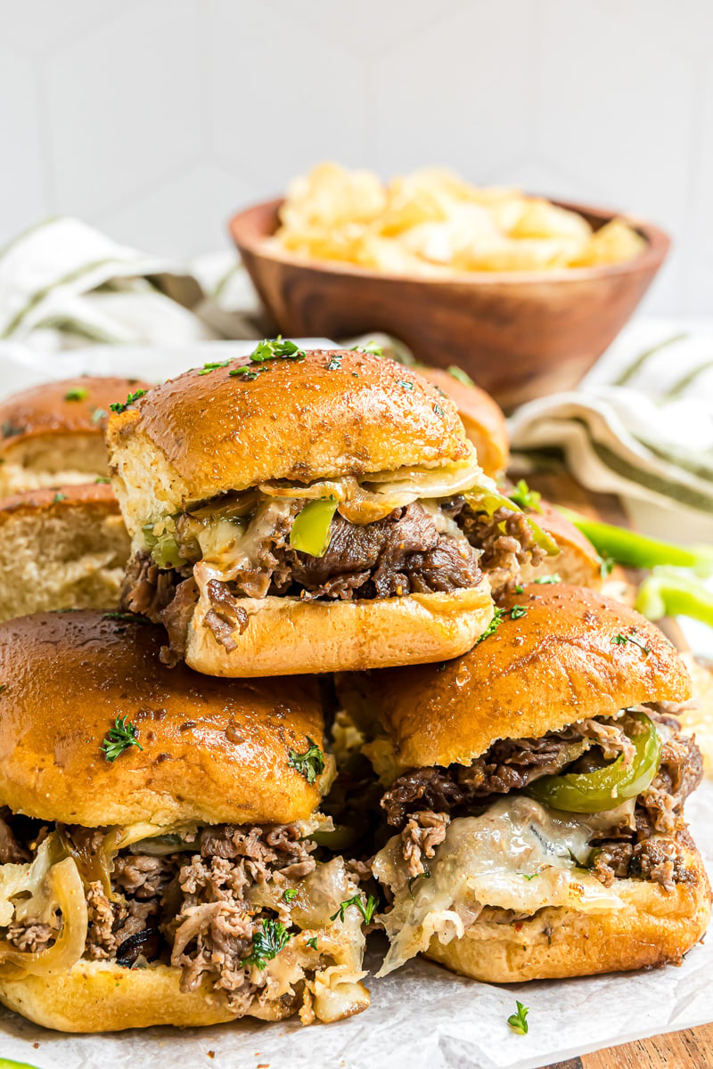 Philly cheesesteak sliders stacked on a white plate.