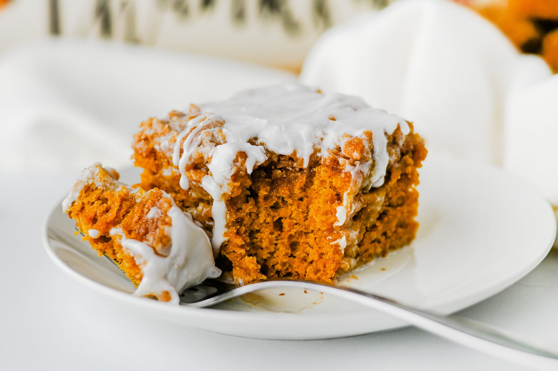 Forkful of pumpkin spice cake on a white plate with remaining piece of cake.