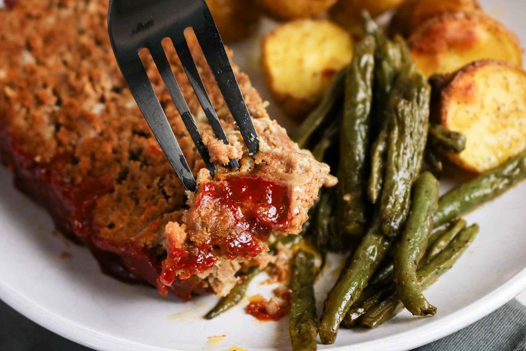 Bite of meatloaf on a fork with veggies on the side.