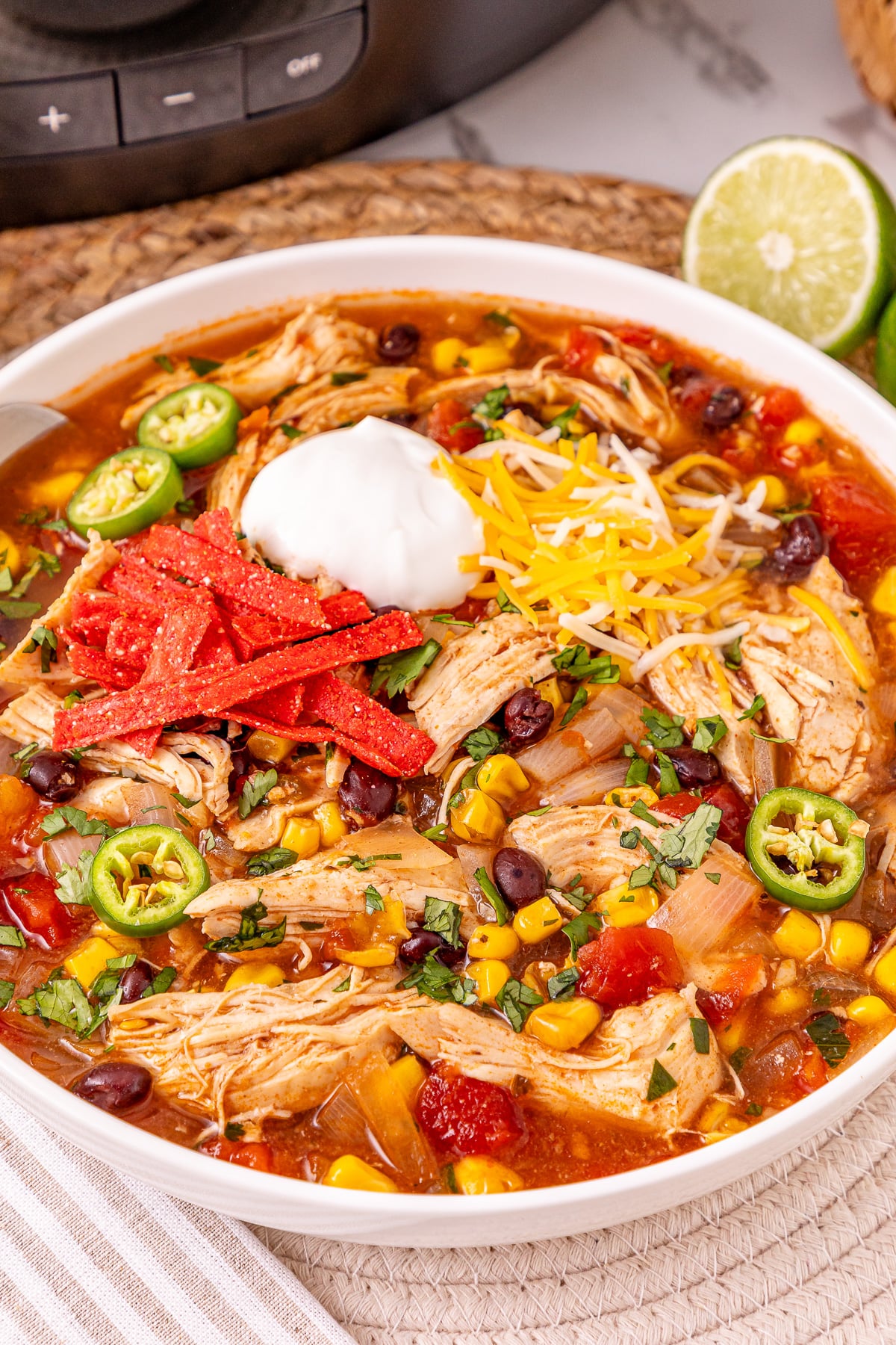 Chicken enchilada casserole in a white oblw, garnished with tortilla strips, sour cream and sliced jalapenos.