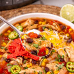 Spoonful of chicken enchilada soup held over bowl of soup.