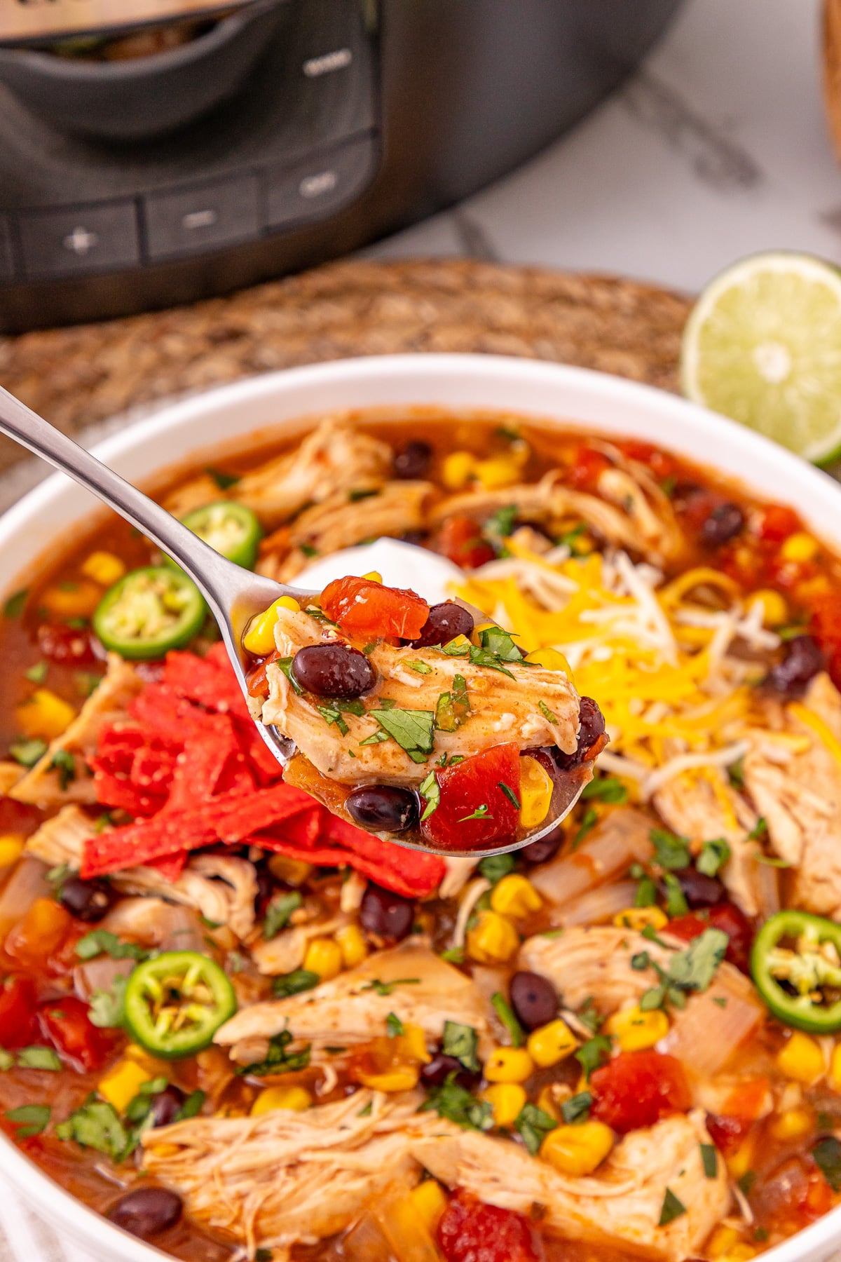 Spoonful of chicken enchilada soup held over bowl of soup.