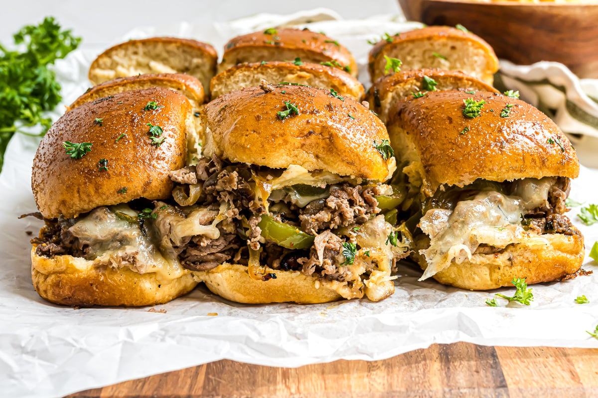 Side view of philly cheesteak sliders on parchment lined baking sheet.