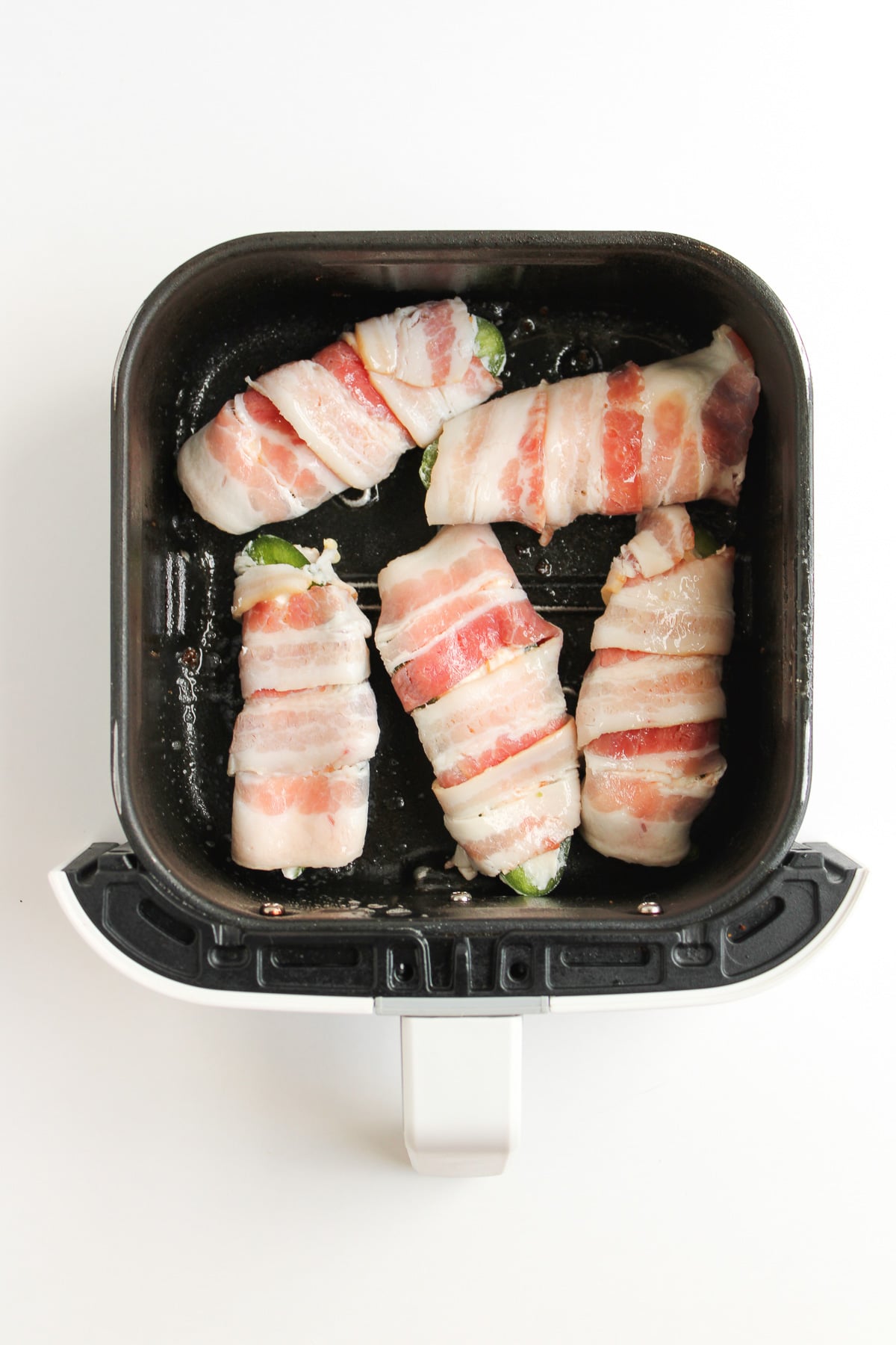 Bacon wrapped jalapeno poppers in air fryer cooking.