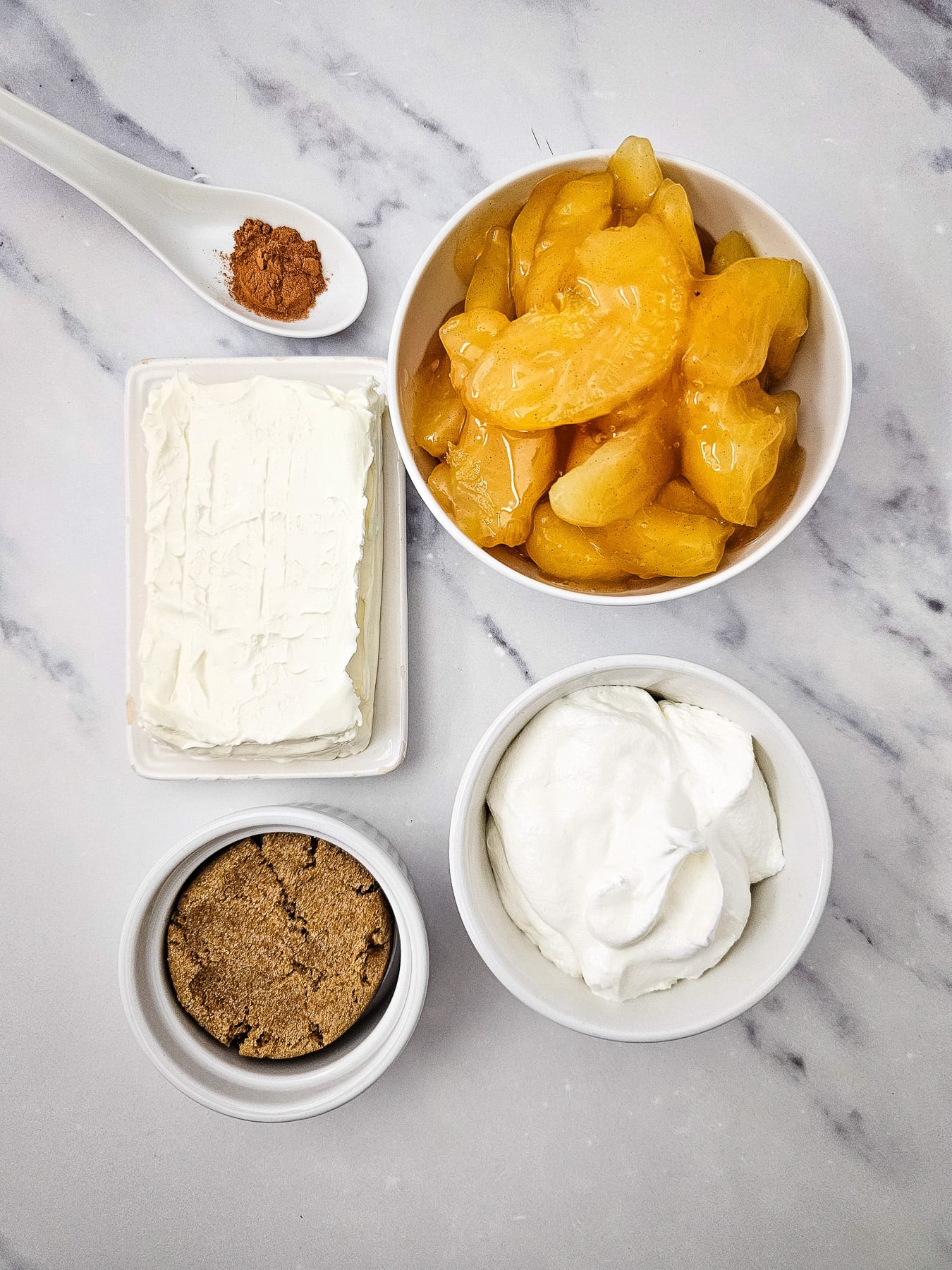 Ingredients for apple pie dip in small bowls on kitchen counter in preparation for the recipe.