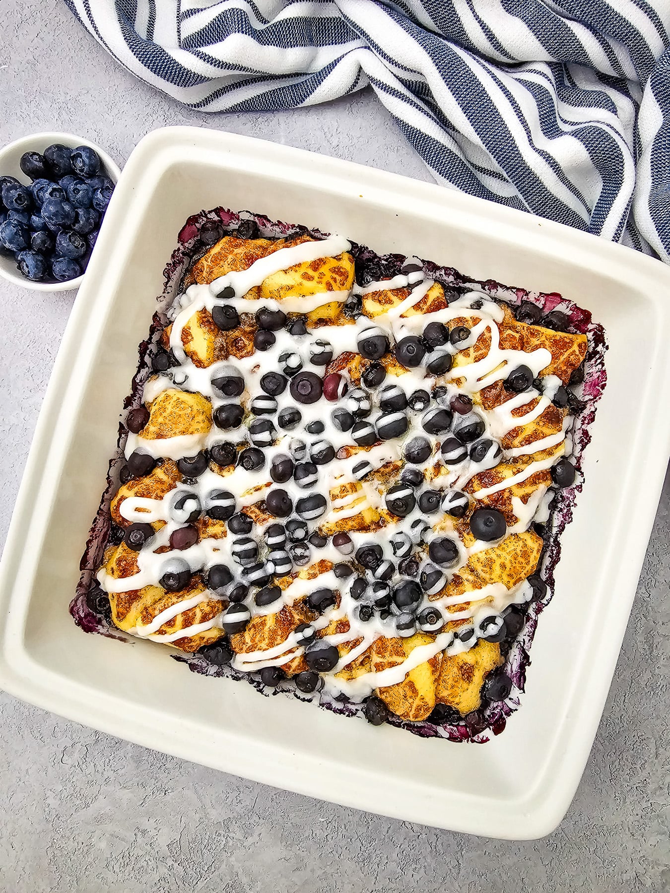Baked cinnamon roll casserole is drizzled with icing from the cinnamon roll tube.