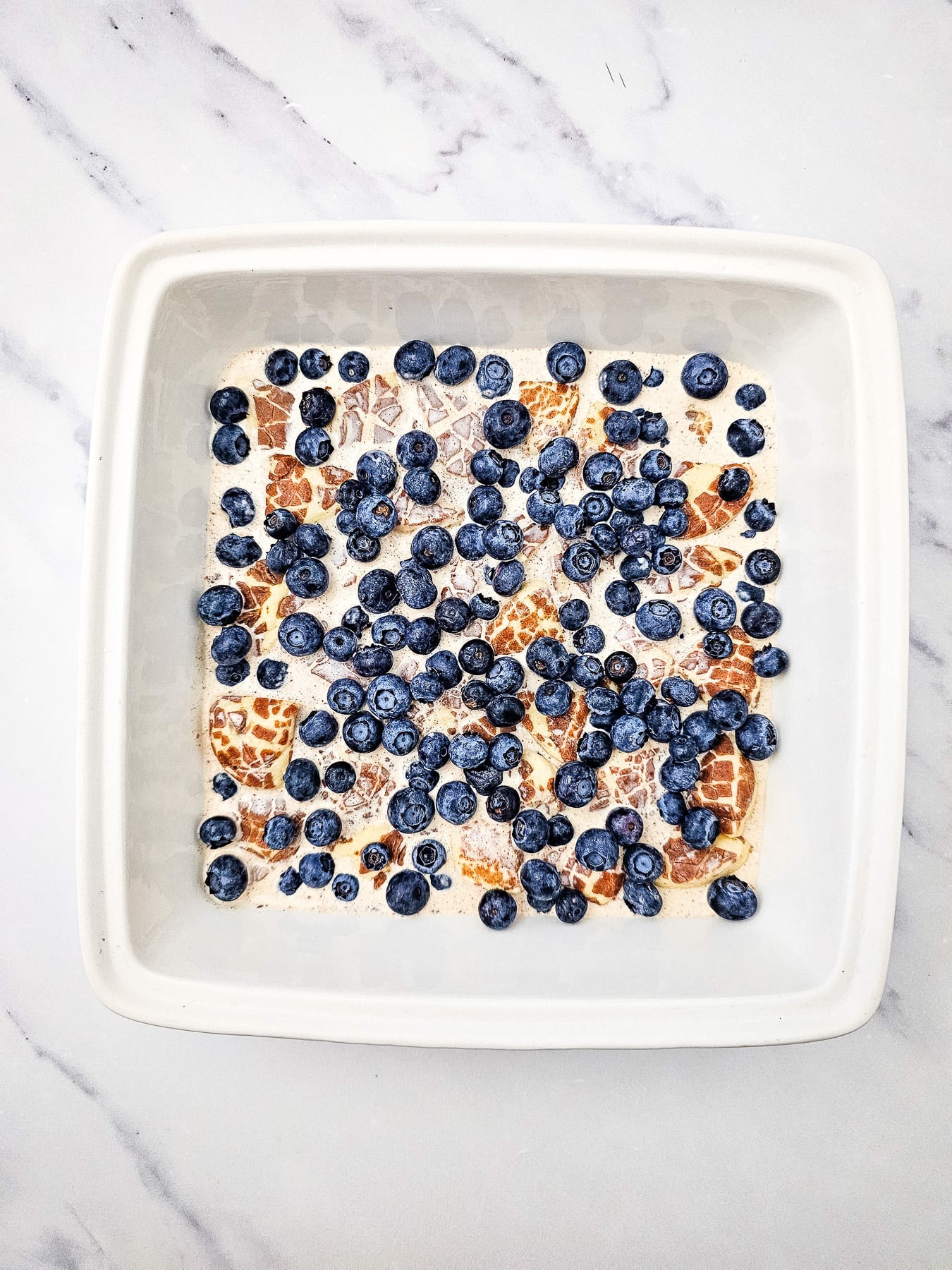 Fresh blueberries are sprinkled on top of the cinnamon roll mixture in baking dish.