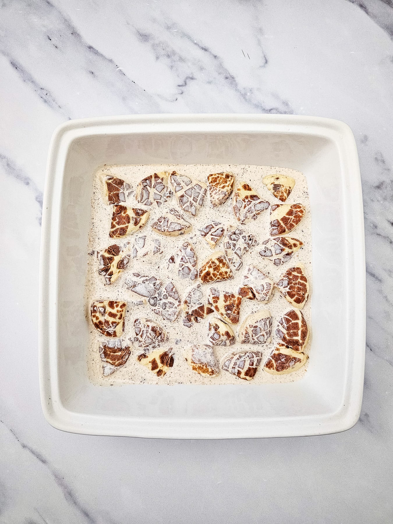 Cream mixture is poured on top of cinnamon rolls in baking dish.,