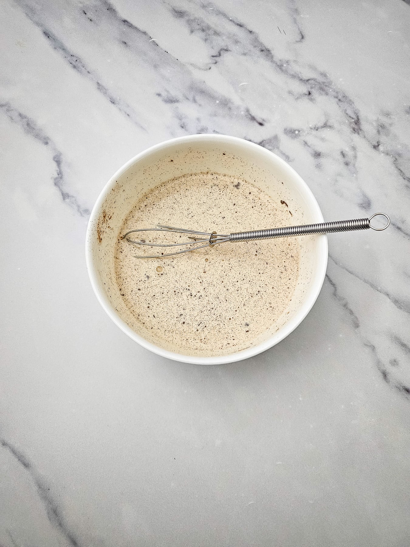 Heavy cream, vanilla extract and ground cinnamon in glass baking dish with whisk.