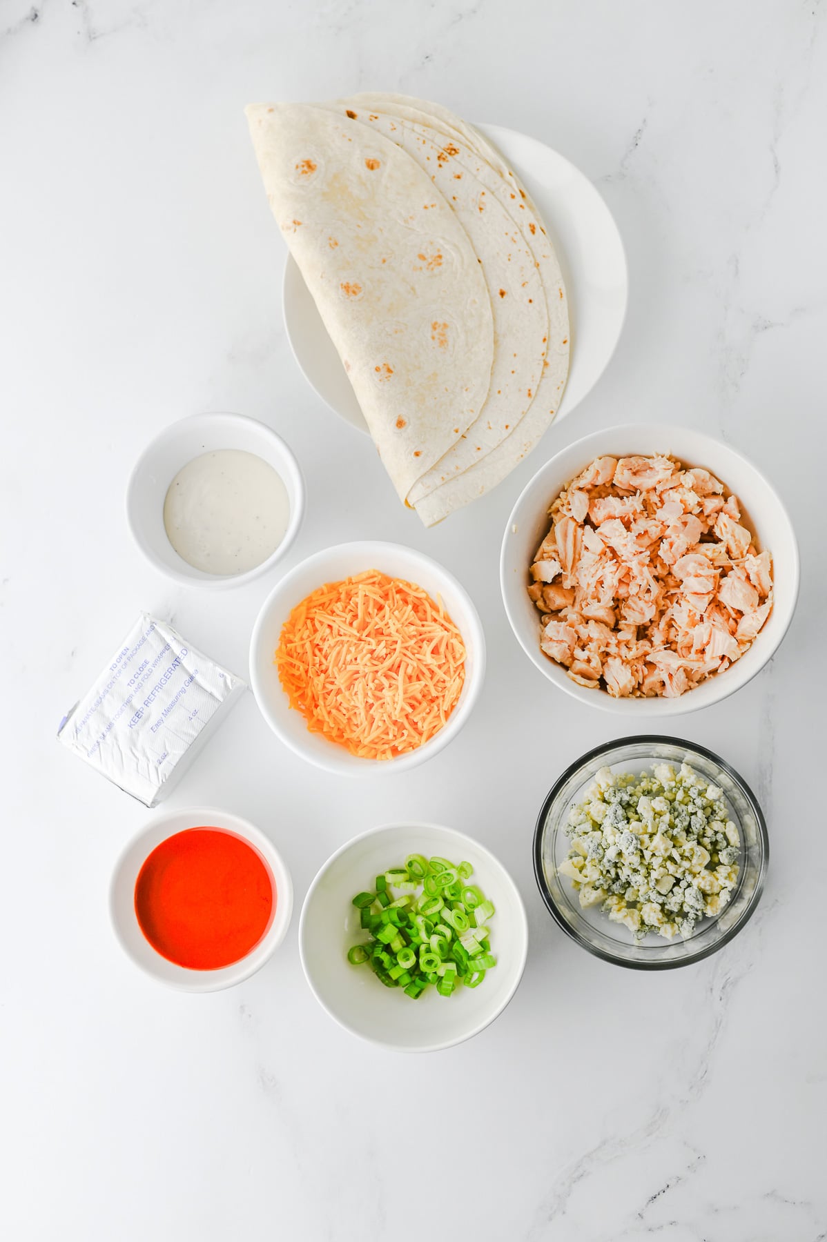 Buffalo chicken pinwheels ingredients in small bowls on counter in preparation for the recipe.