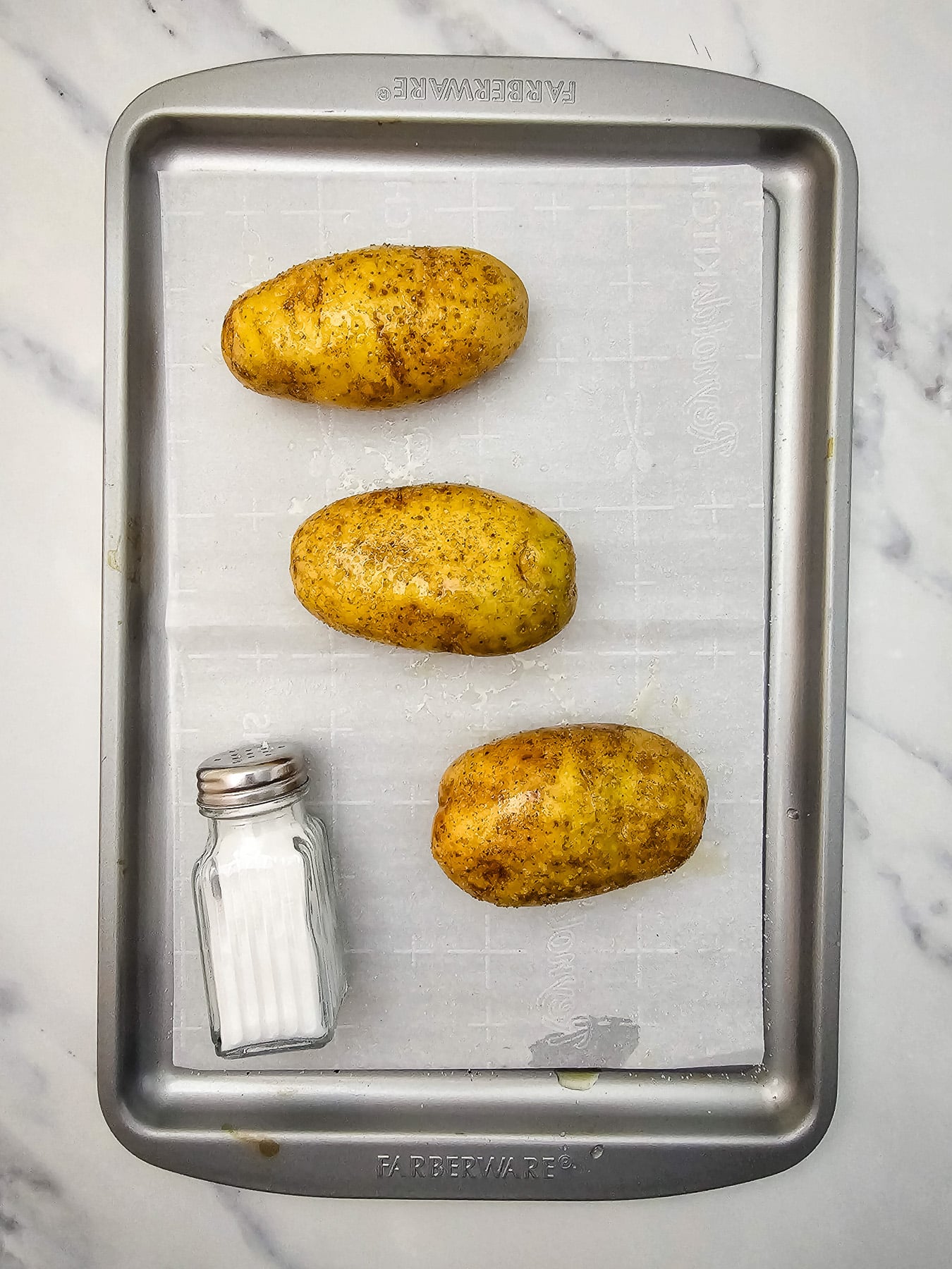 Baking potatoes on baking sheet, pierced with a fork.