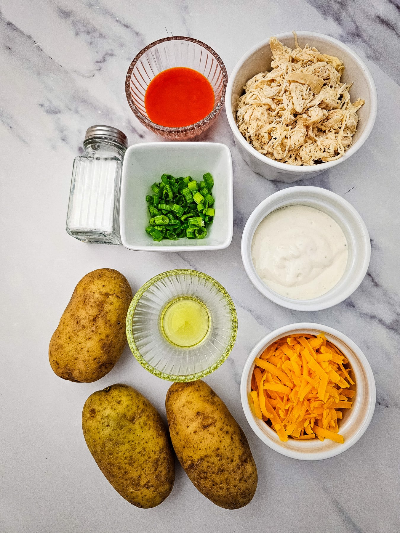 Buffalo chicken potato skins ingredients in small bowls on counter.