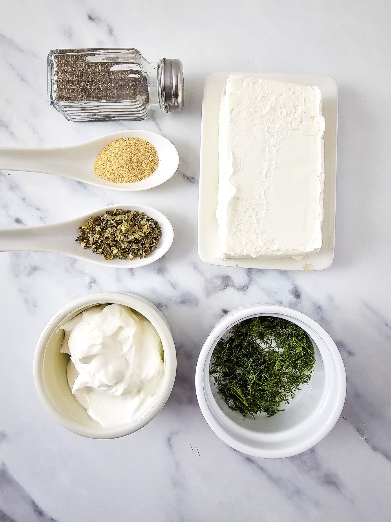 Ingredients for ceram cheese veggie dip laid out in small bowls on kitchen counter in preparation for the recipe.