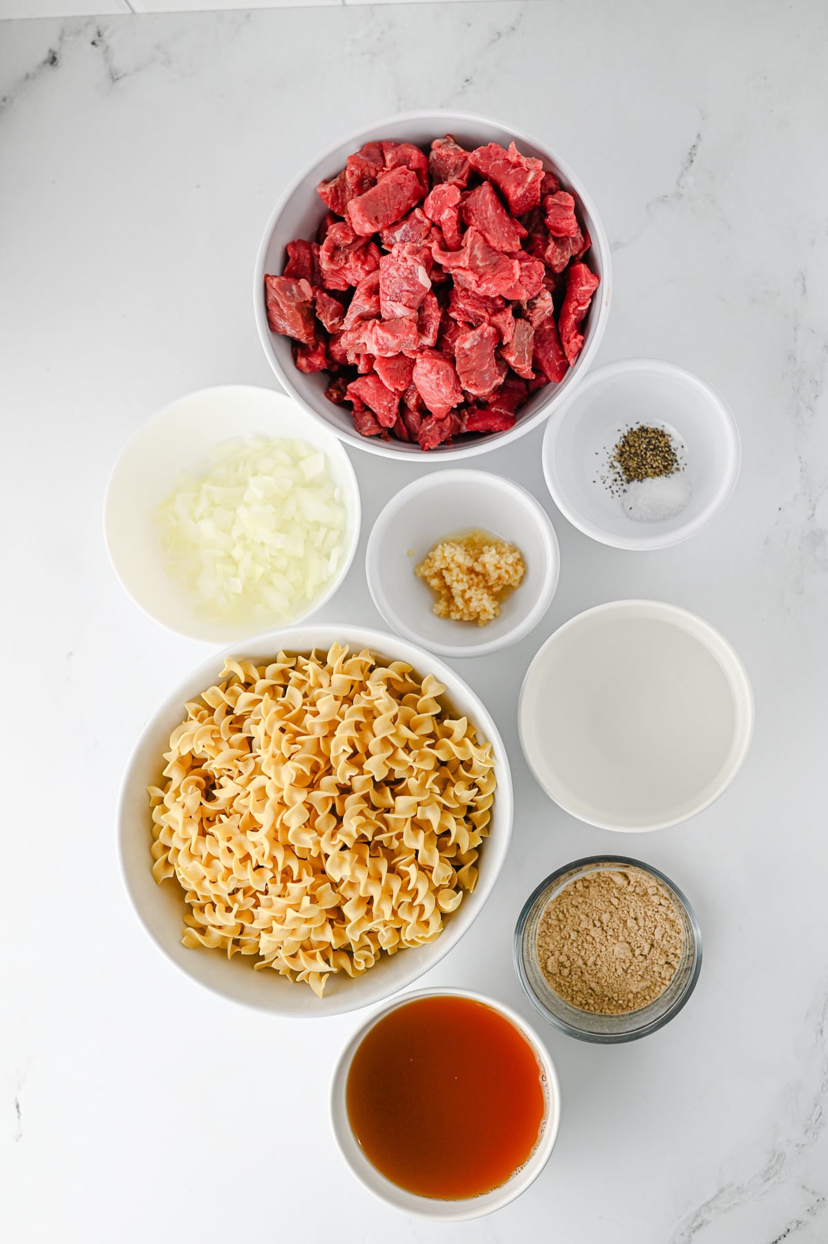 Ingredients for crockpot beef and noodles laid out in small bowls on kitchen counter.