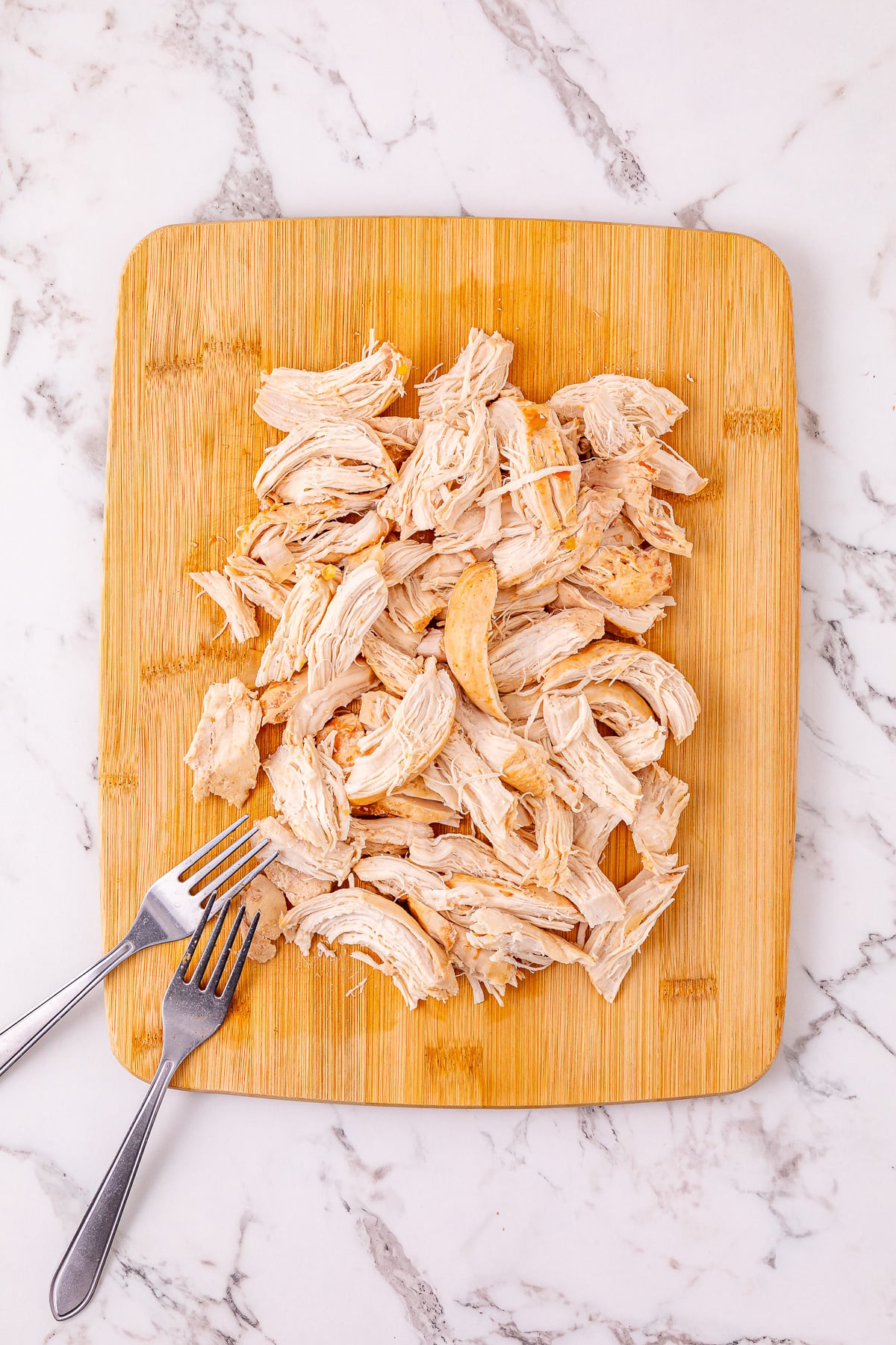 Shredded chicken on a wooden cutting board.