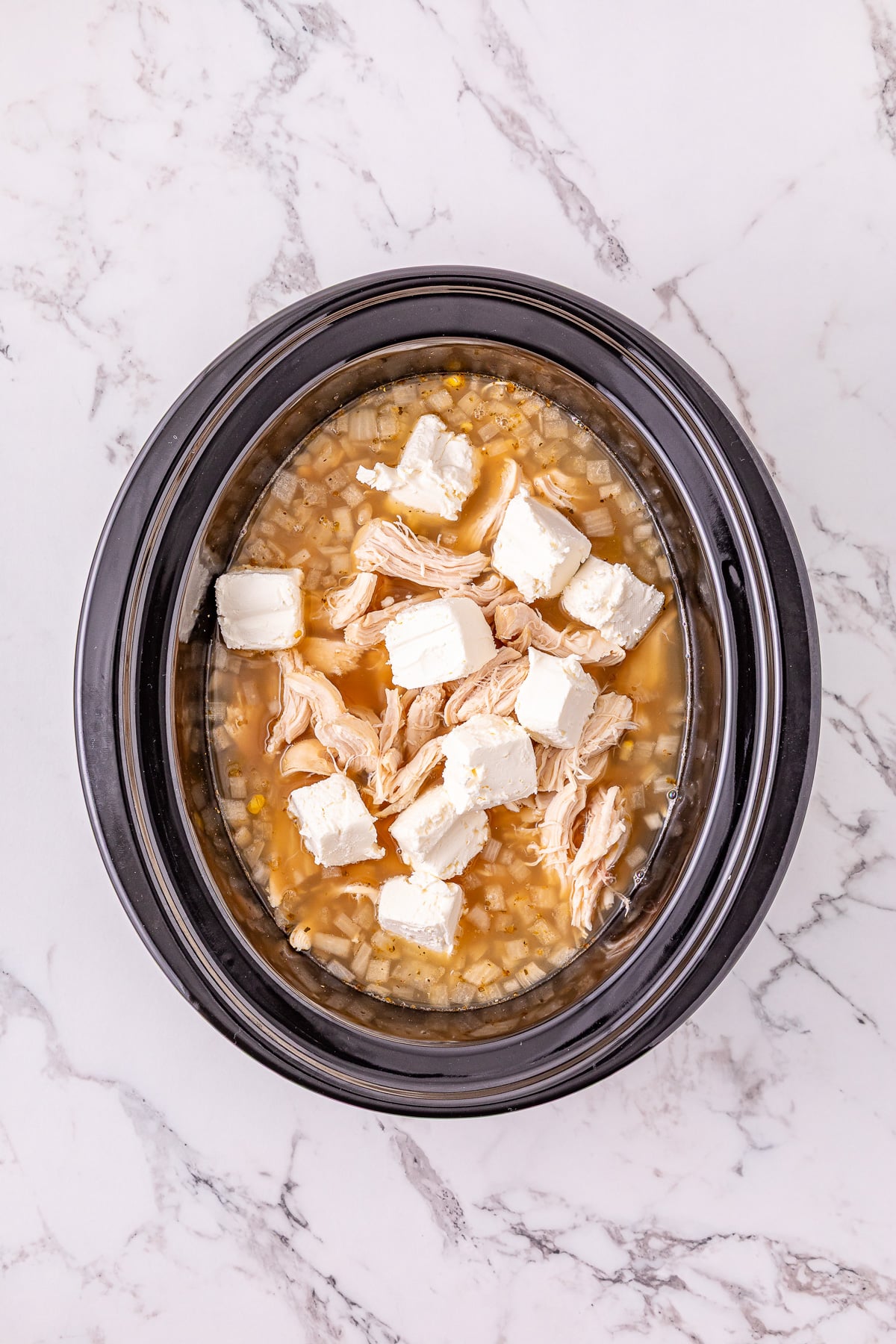 Chicken is returned to the crockpot, then cubed cream cheese is added to the top.
