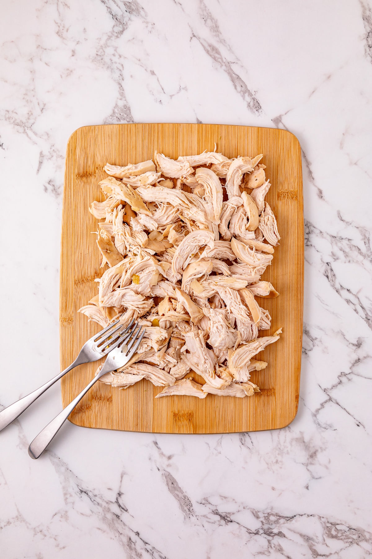 Shredded chicken on wooden cutting board.