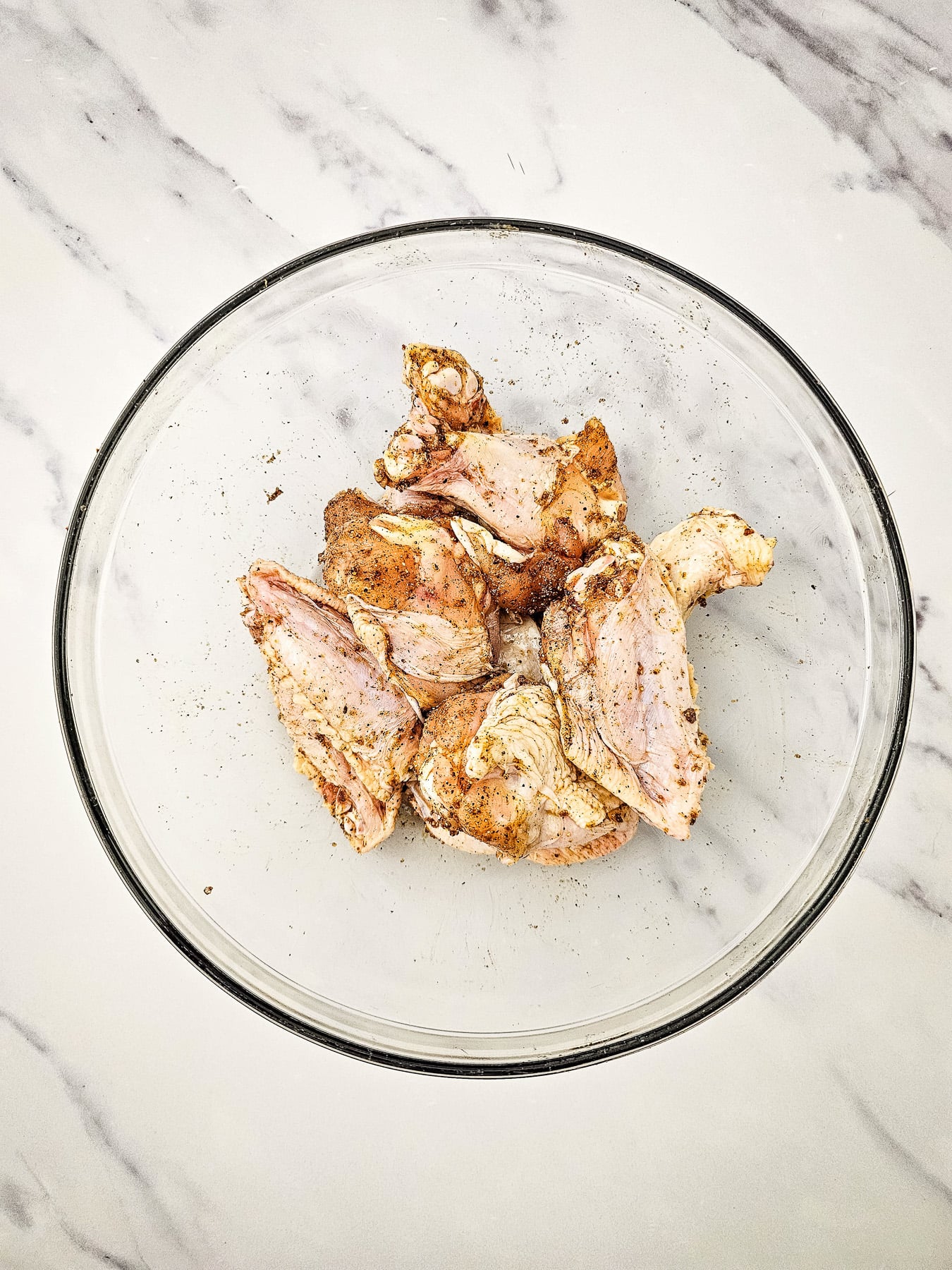 Chicken wings in bowl with seasoning.
