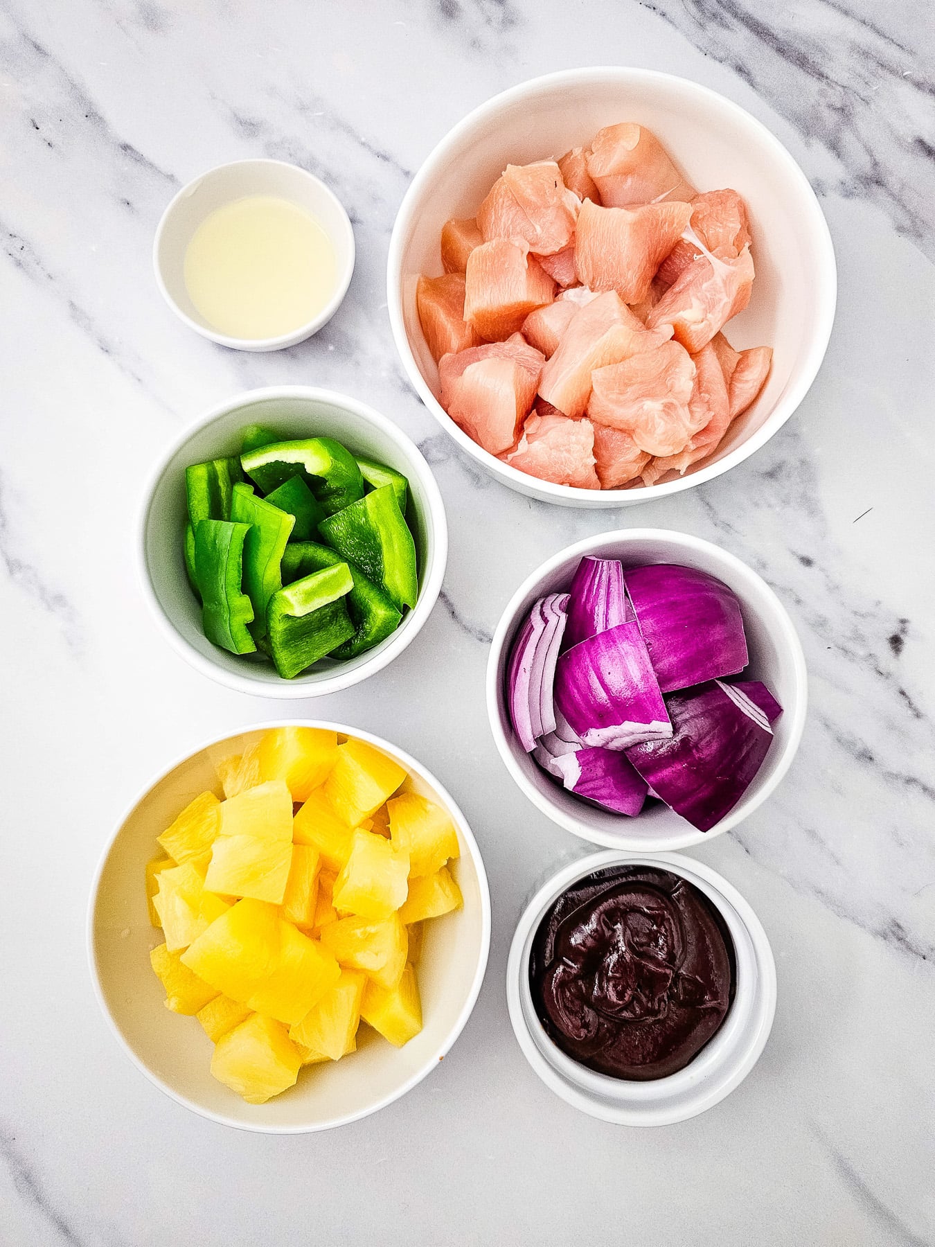 Ingredients for grilled chicken and pineapple kabobs in small bowls on counter.