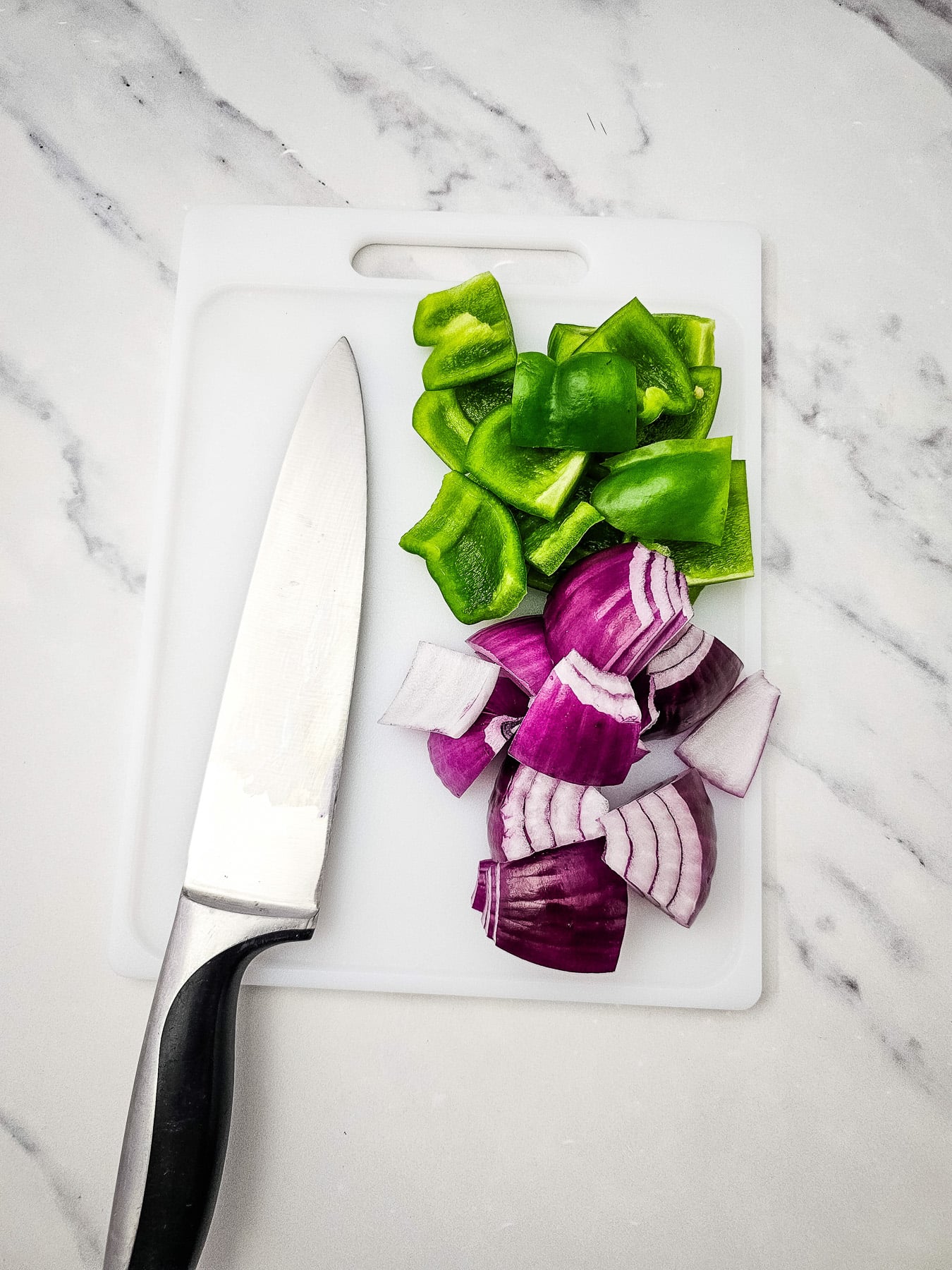 Chopped peppers and red onions on a cutting board.