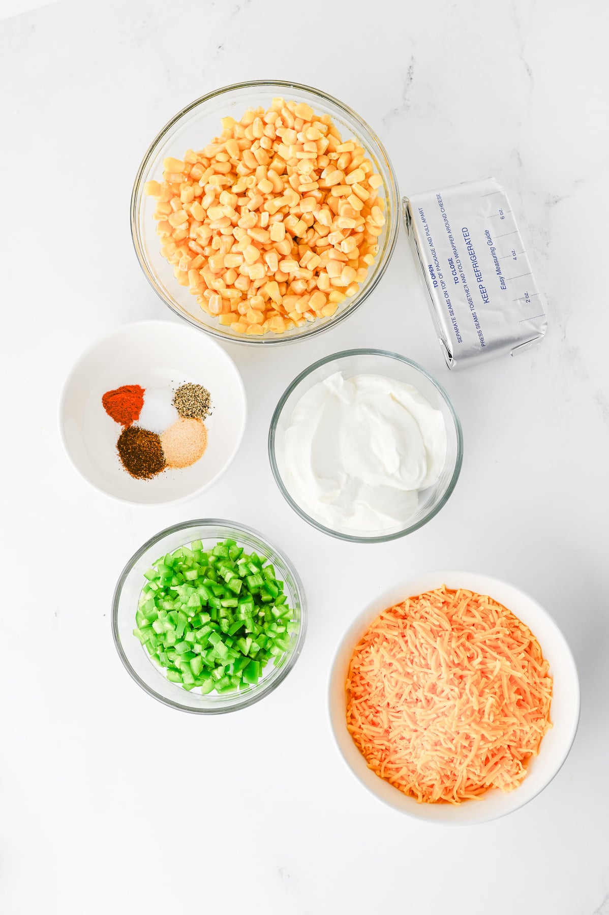 Ingredients for hot jalapeno corn dip in small bowls on kitchen counter.