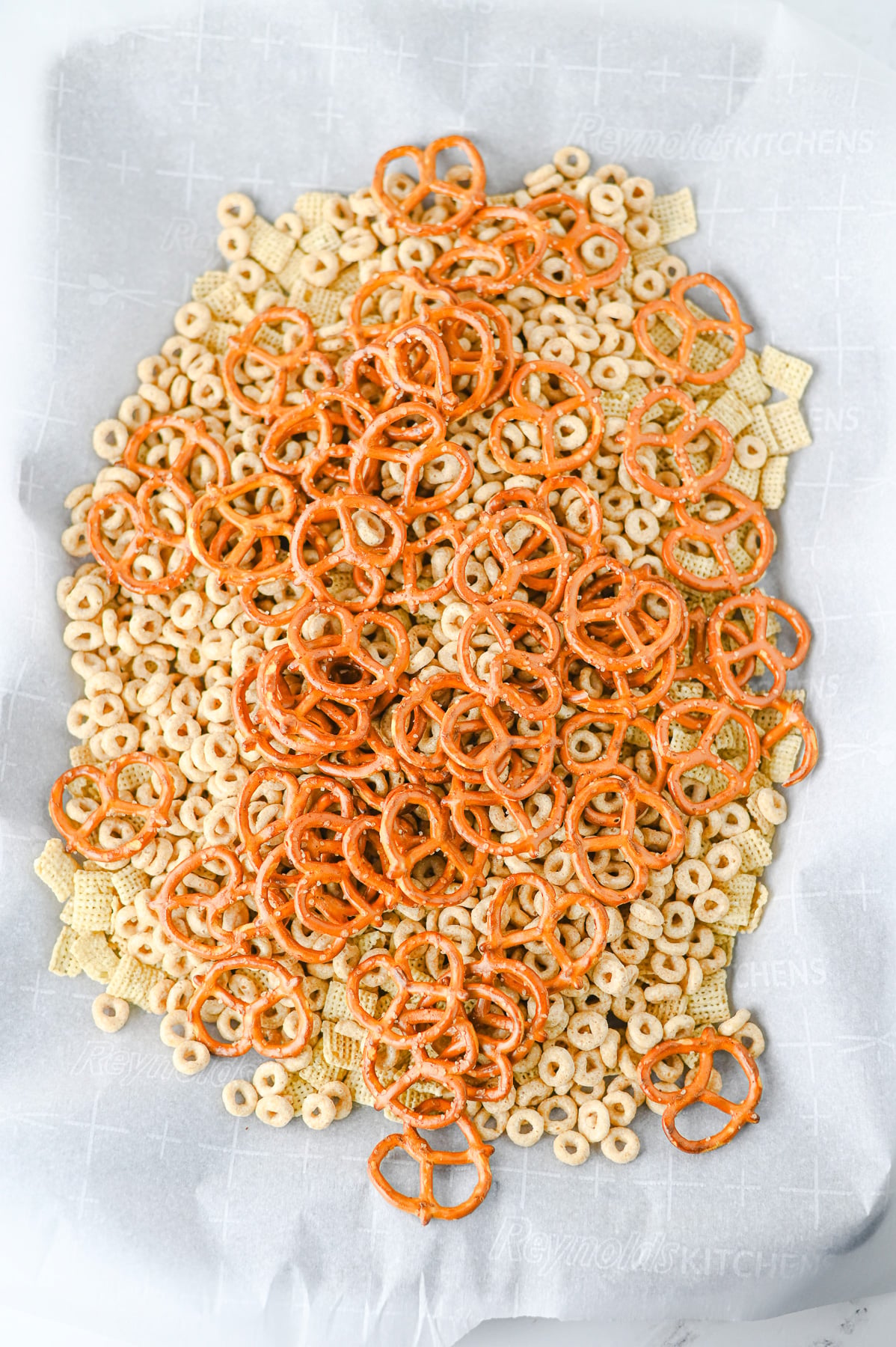 Cereal and pretzels on parchment lined baking sheet.