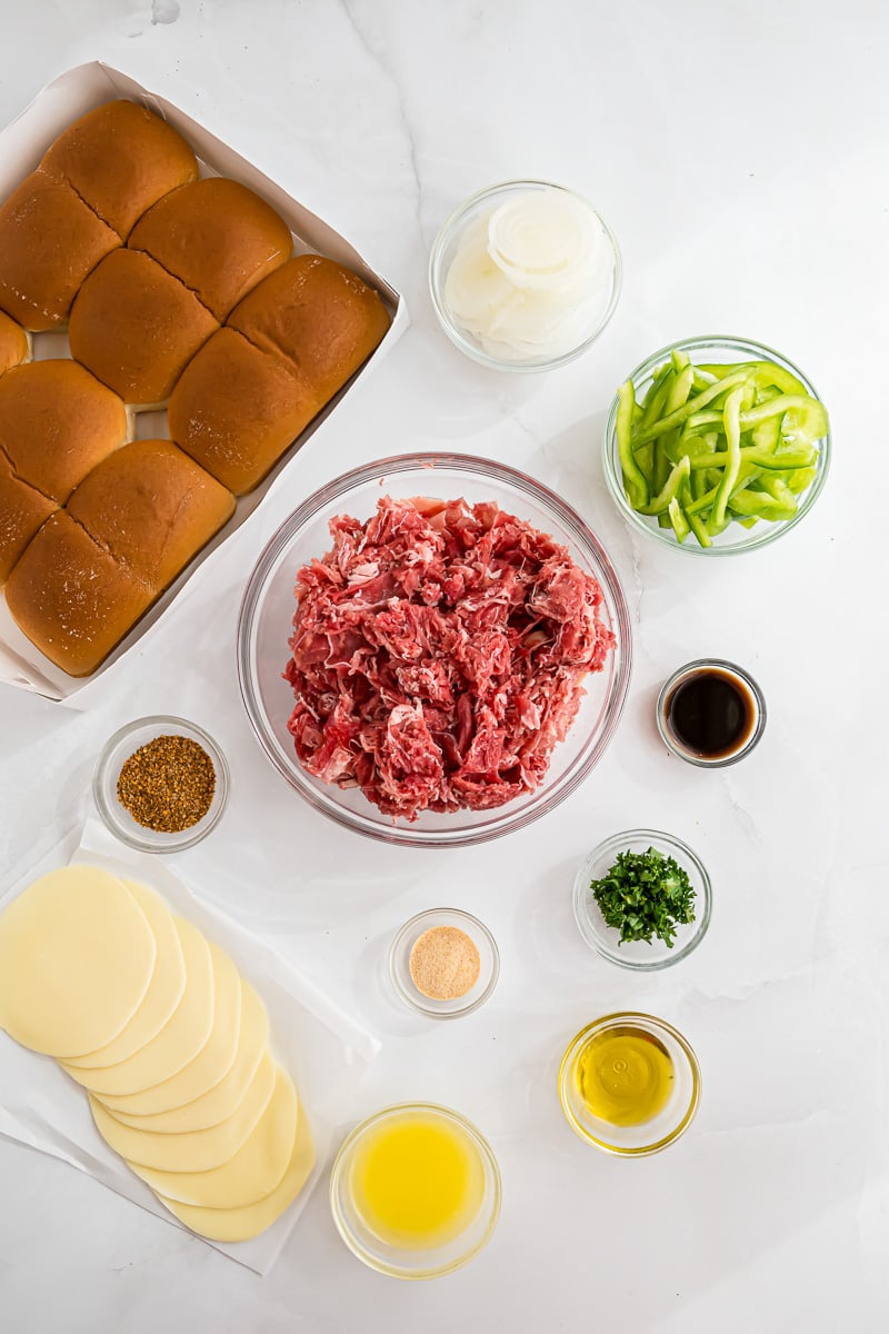 Philly cheesesteak sliders ingredients in small bowls on kitchen counter.