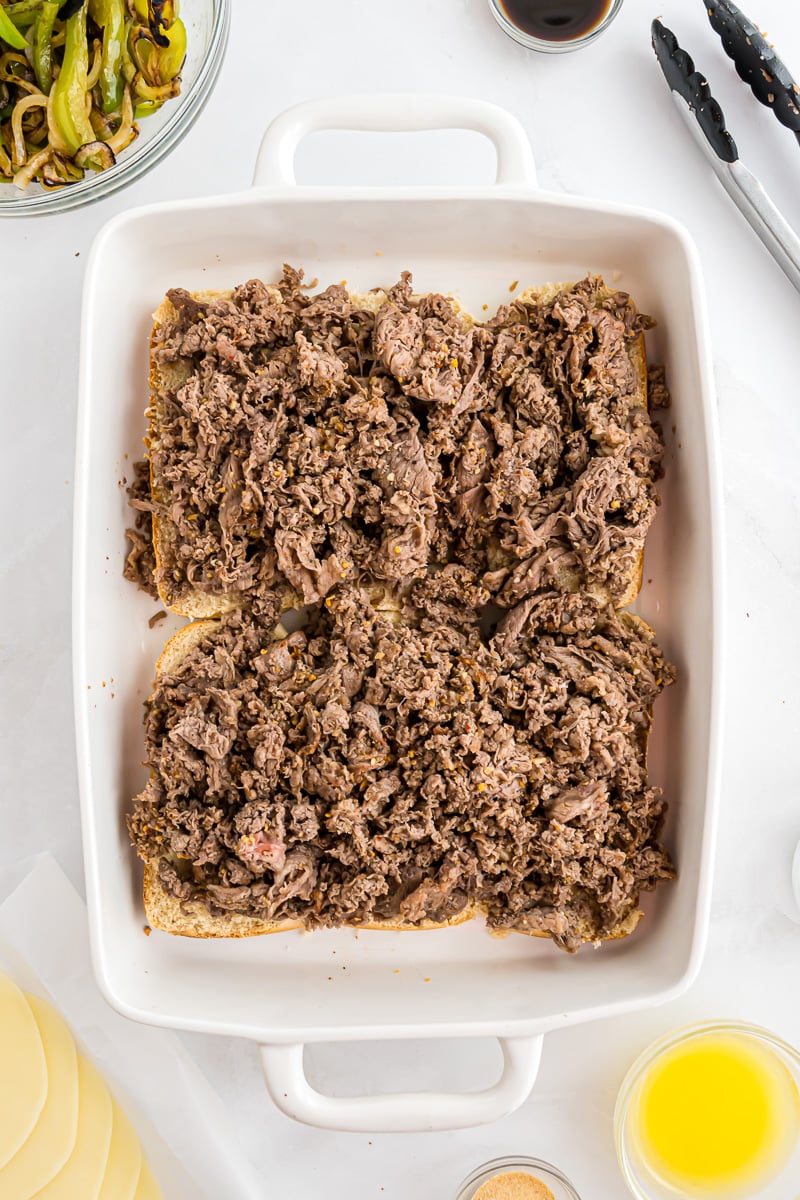 Sliced slider buns are topped with the shaved cooked beef.