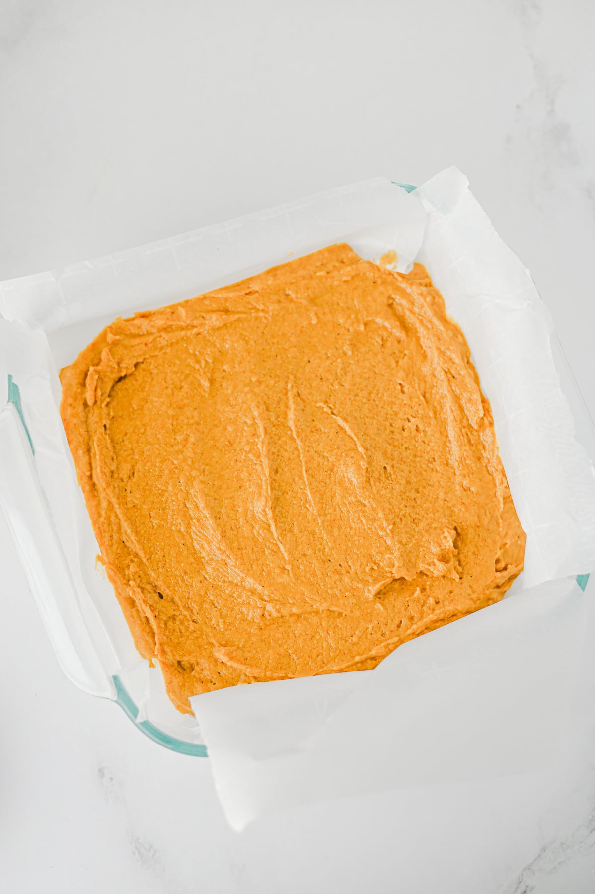 Pumpkin batter is spread in bottom of square baking dish.