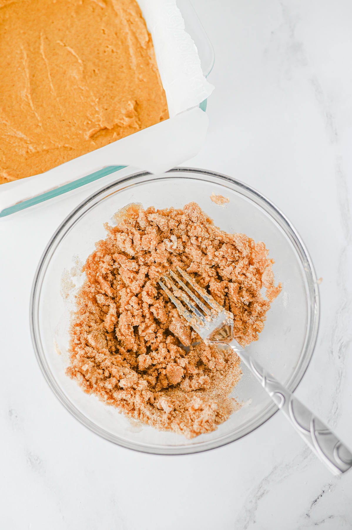 Crumble topping is mixed with a fork in a glass bowl.