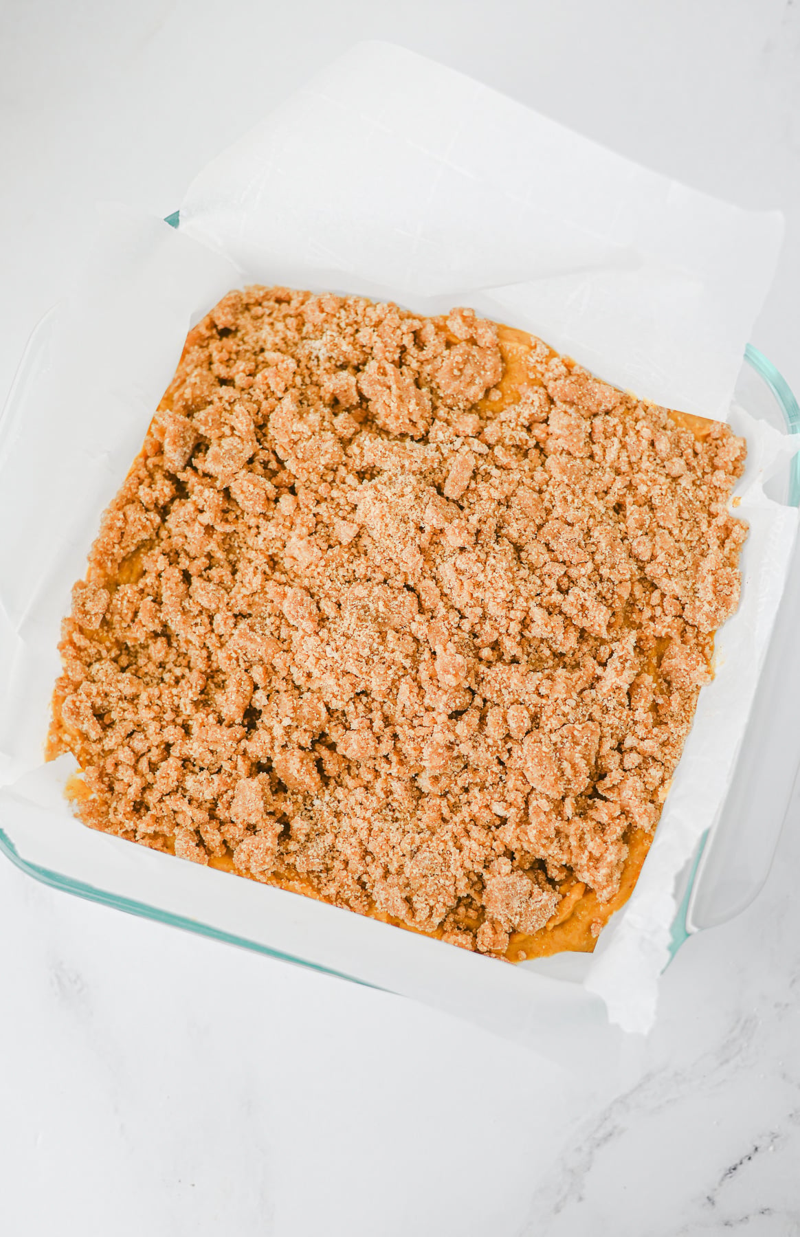 Crumb topping is sprinkled on top of pumpkin cake batter in baking dish.