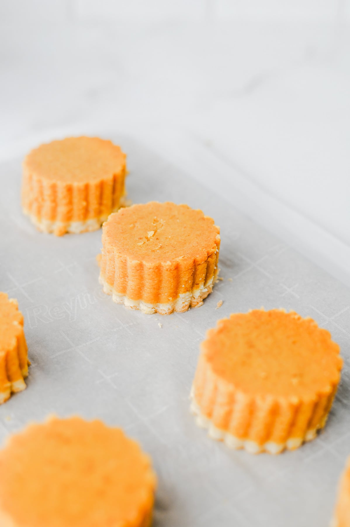 Circle-cut pumpkin pie bites on parchment lined baking sheet.