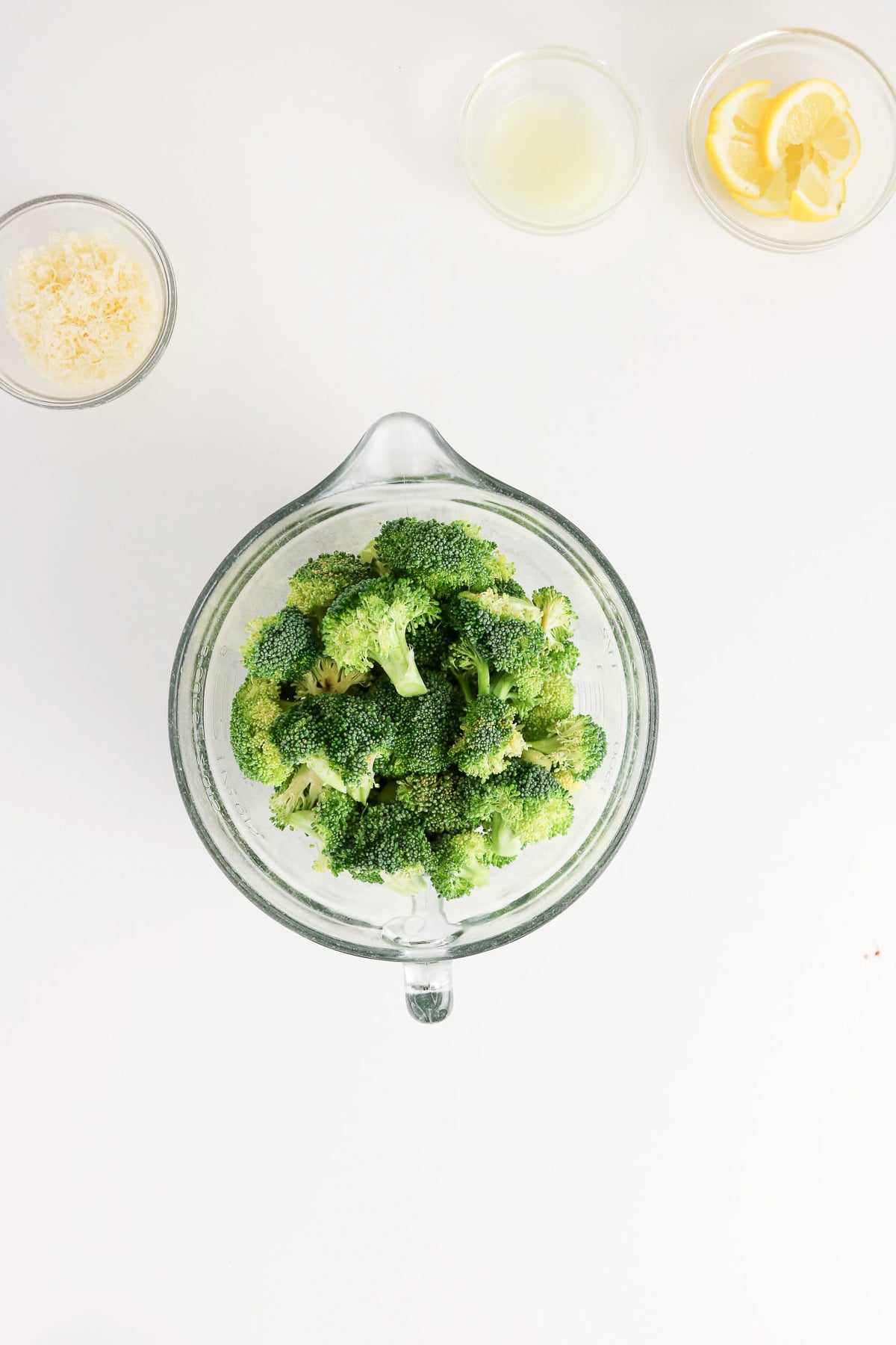 Broccoli in measuring cup is drizzled with olive oil.