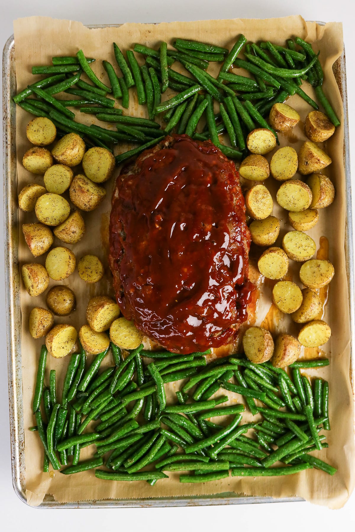 Unbaked potatoes and green beans surrounding the meatloaf.