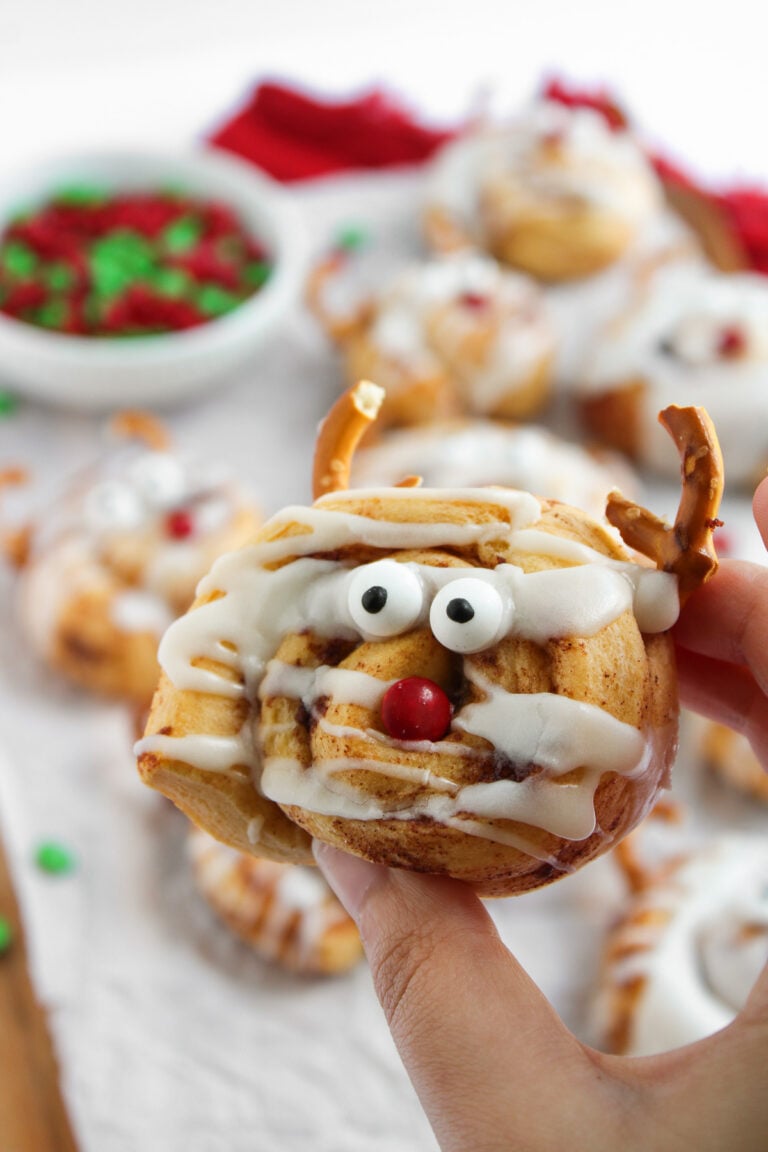 Reindeer cinnamon roll held up over baking dish.
