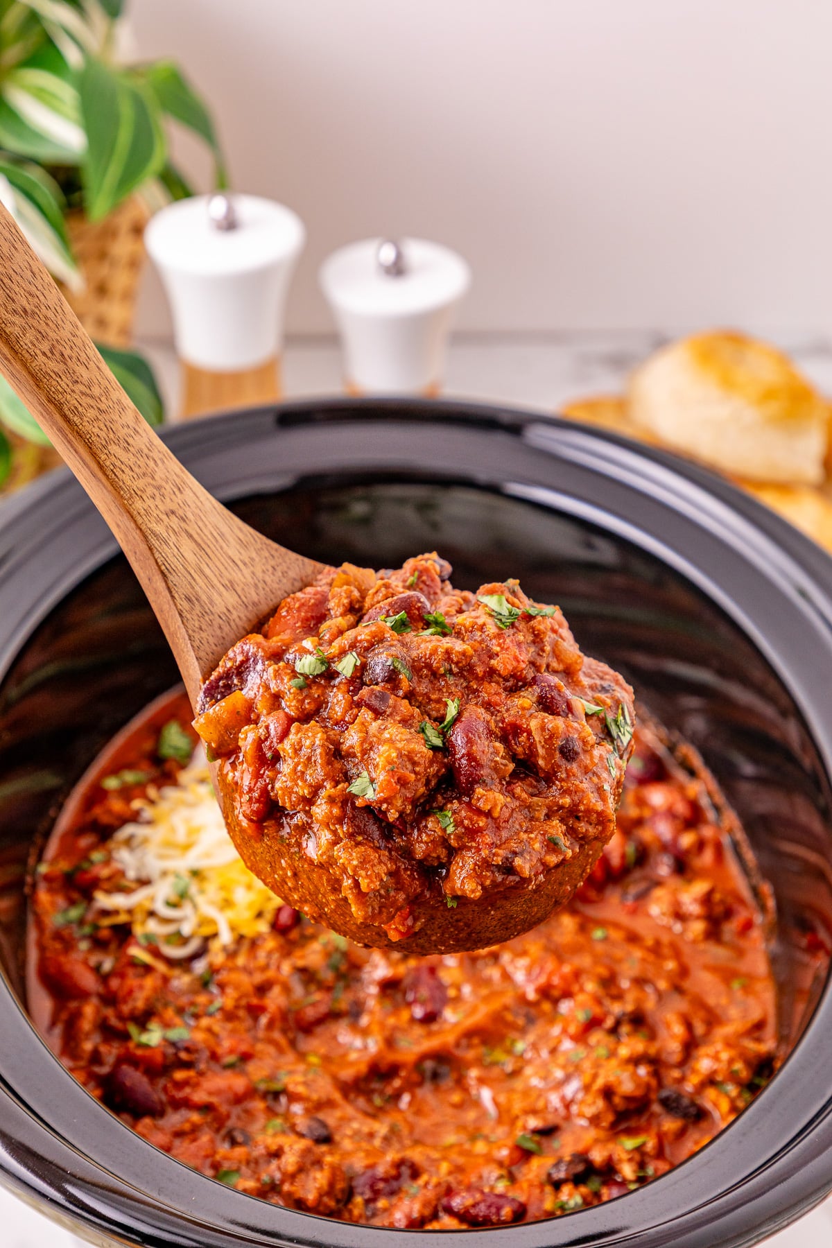 Scoop of crockpot chili on wooden spoon ready to be served.