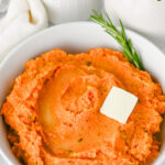 Mashed sweet potatoes with a dollop of butter in a white bowl.