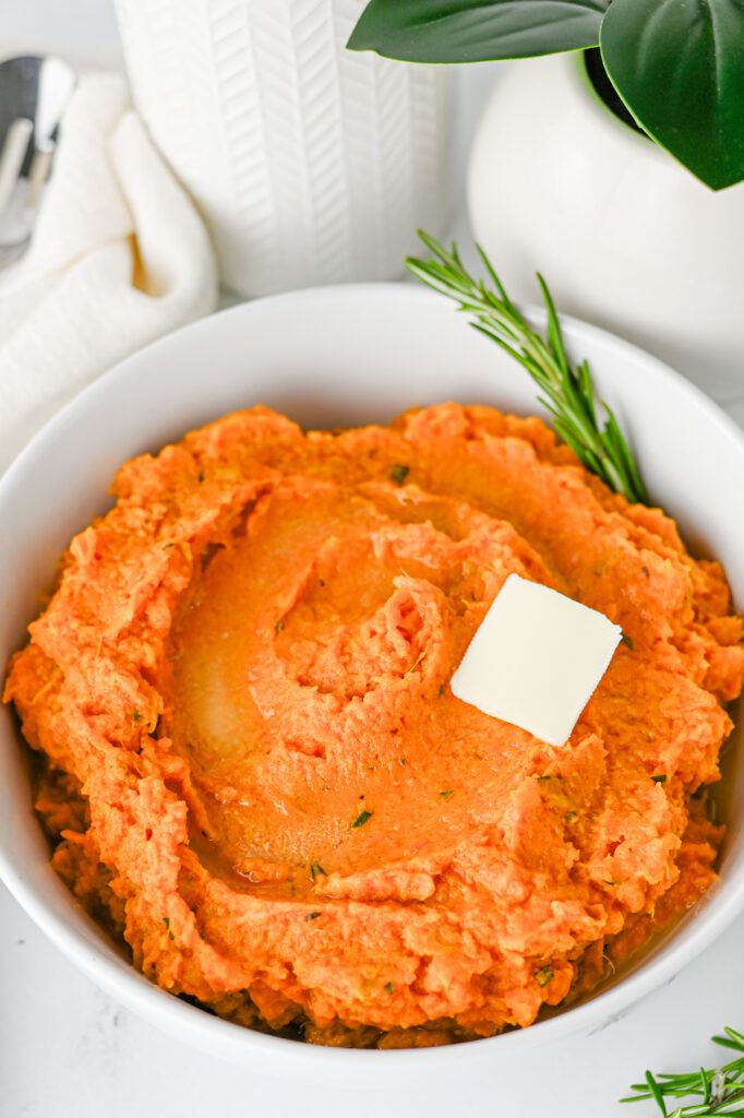 Mashed sweet potatoes with a dollop of butter in a white bowl.