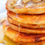 Fluffy pumpkin pancakes with maple syrup and walnuts served on a white plate for breakfast.
