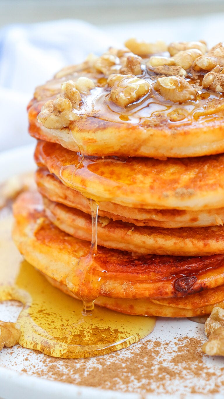Fluffy pumpkin pancakes with maple syrup and walnuts served on a white plate for breakfast.