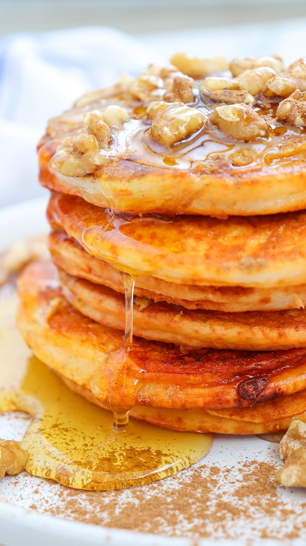 Fluffy pumpkin pancakes with maple syrup and walnuts served on a white plate for breakfast.