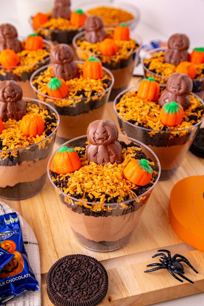 Pumpkin patch dirt cups single-serve desserts on a wooden tray for a fall party.