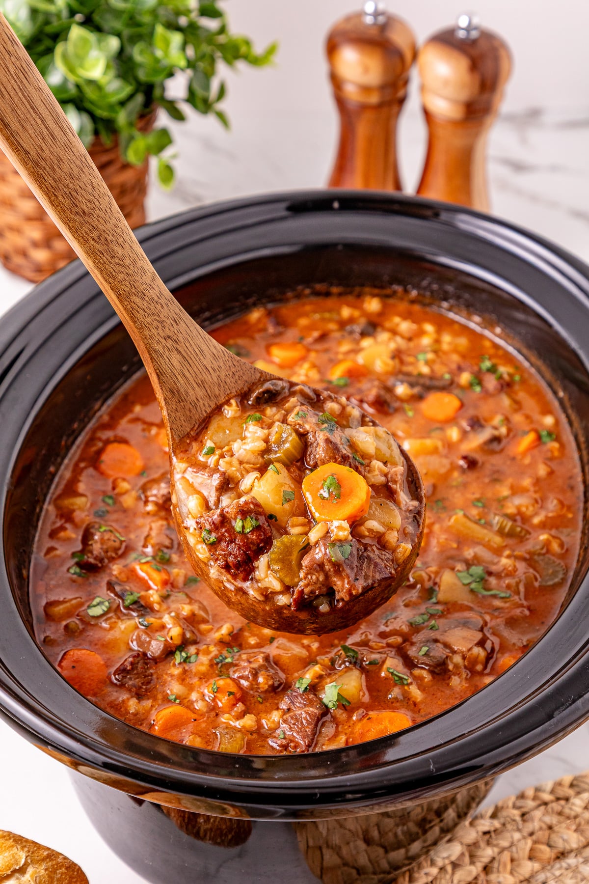Crockpot beef barley soup scooped up in a ladle held over slow cooker.